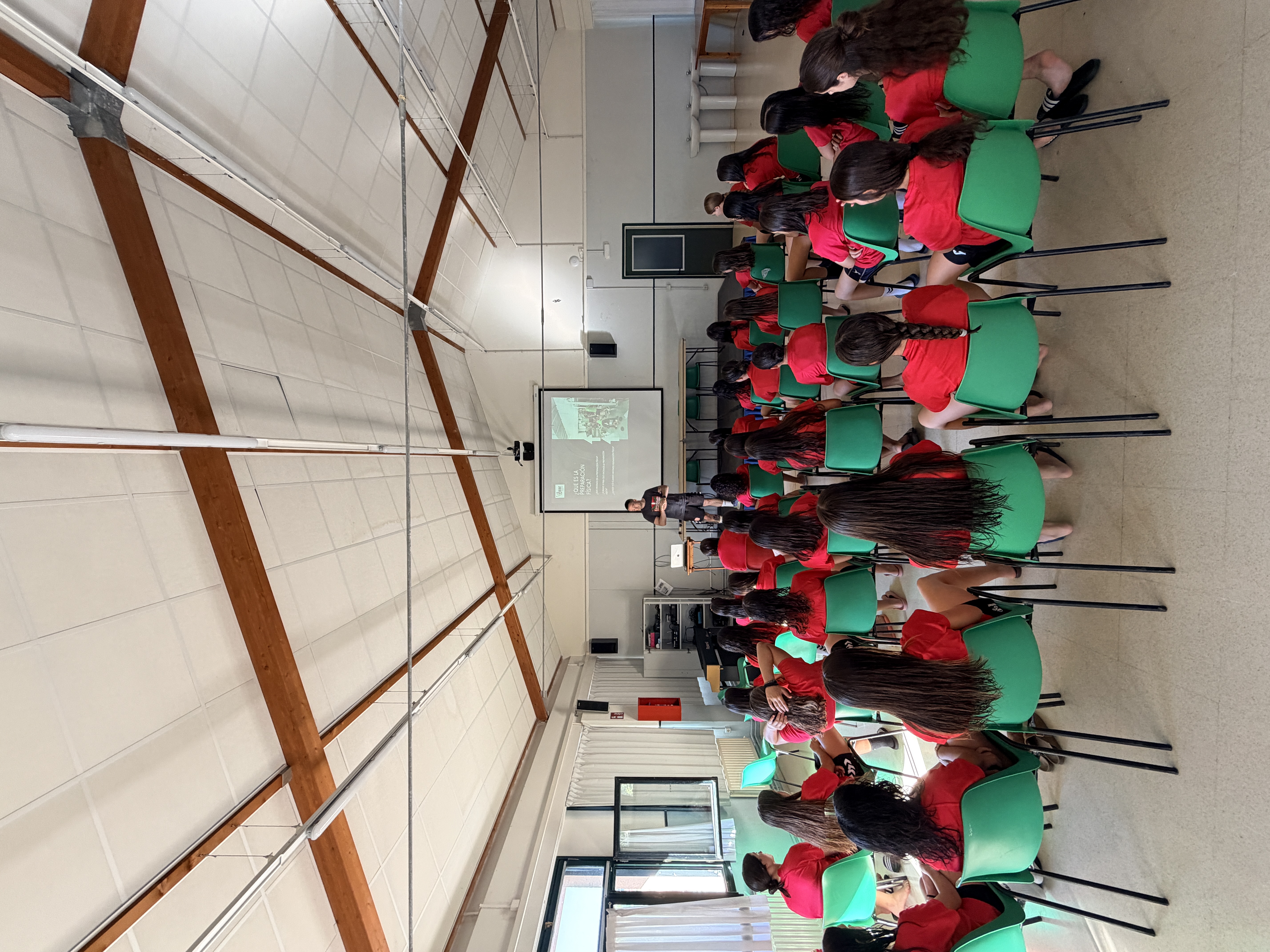 Grupo de jugadoras en camiseta roja asistiendo a una sesión de vídeo y análisis táctico durante el TARE o la Akademia de la Federación Vasca de Balonmano